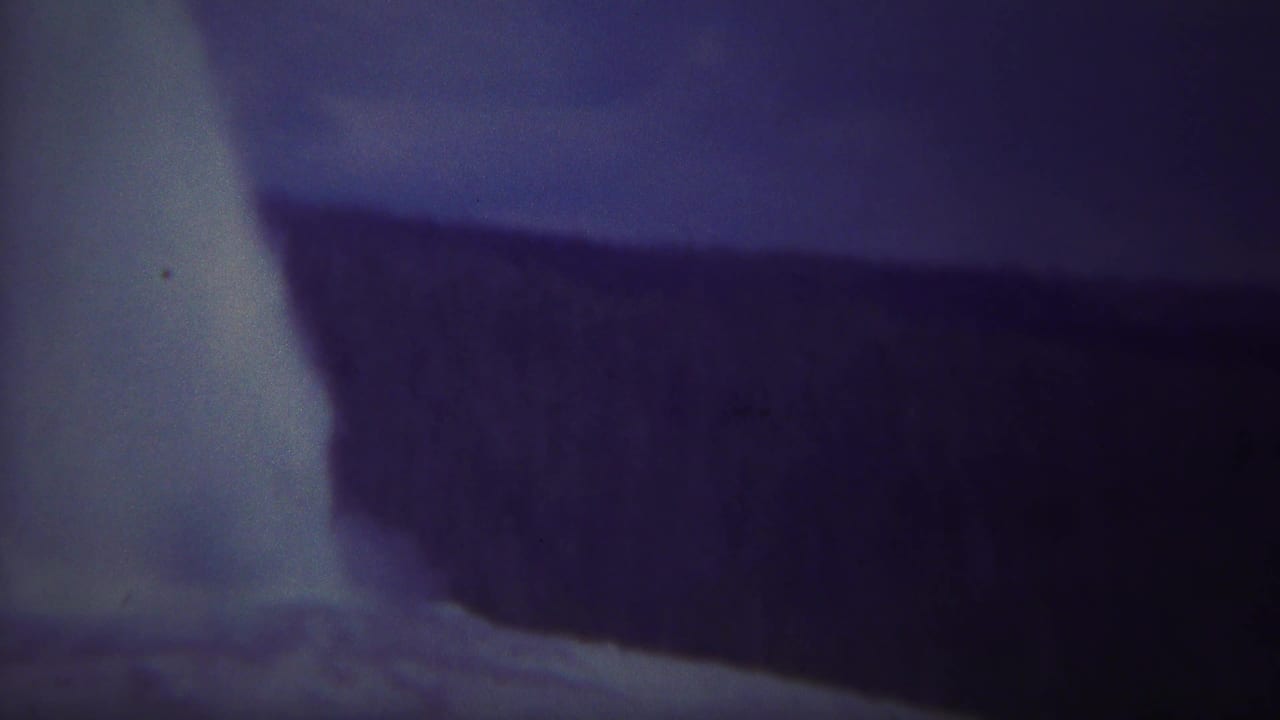 1967 Yellowstone 8mm frame showing pale water falling beside a dark cliff edge with soft focus and aged blue-purple color.