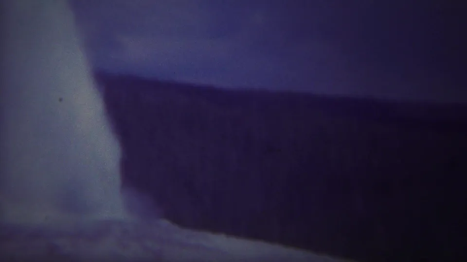 1967 Yellowstone 8mm frame showing pale water falling beside a dark cliff edge with soft focus and aged blue-purple color.