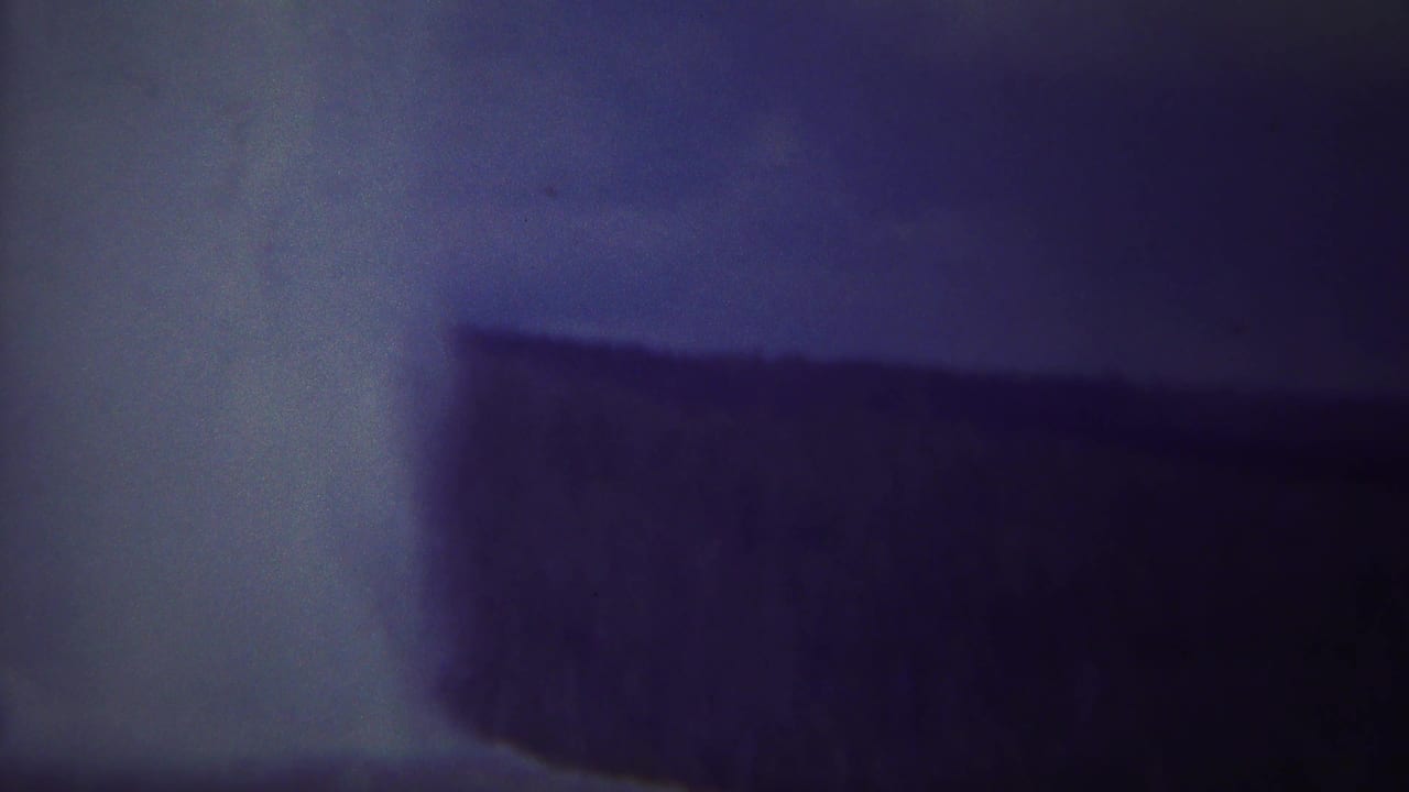 Close view of dark rock and pale falling water with heavy blue-purple cast.