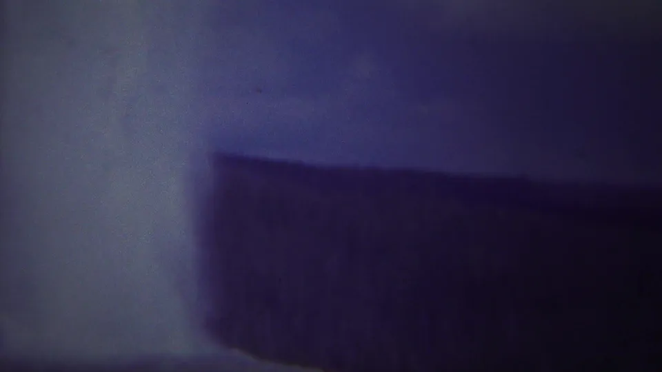 1967 Yellowstone home-movie frame with dark rock faces and pale falling water rendered in aged blue-purple film tones.