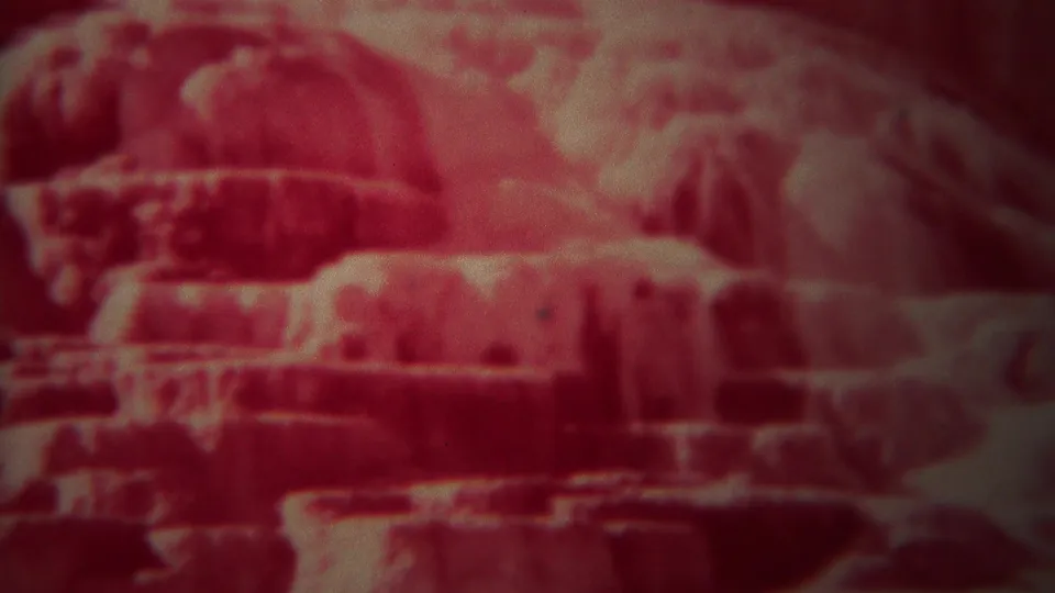1967 Yellowstone home-movie frame showing red-tinted layered rock or mineral ledges in soft focus.