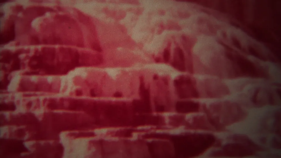Red-shifted 1967 Yellowstone home-movie frame showing layered stone surfaces with a dark recess below.