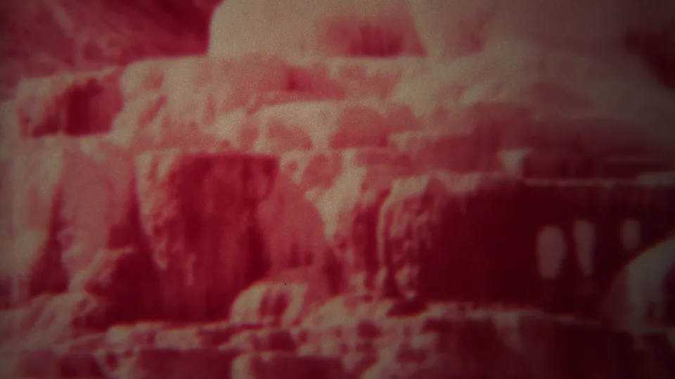 Red-faded 1967 Yellowstone home-movie frame showing rugged canyon terrain, soft focus, and heavy 8mm grain.