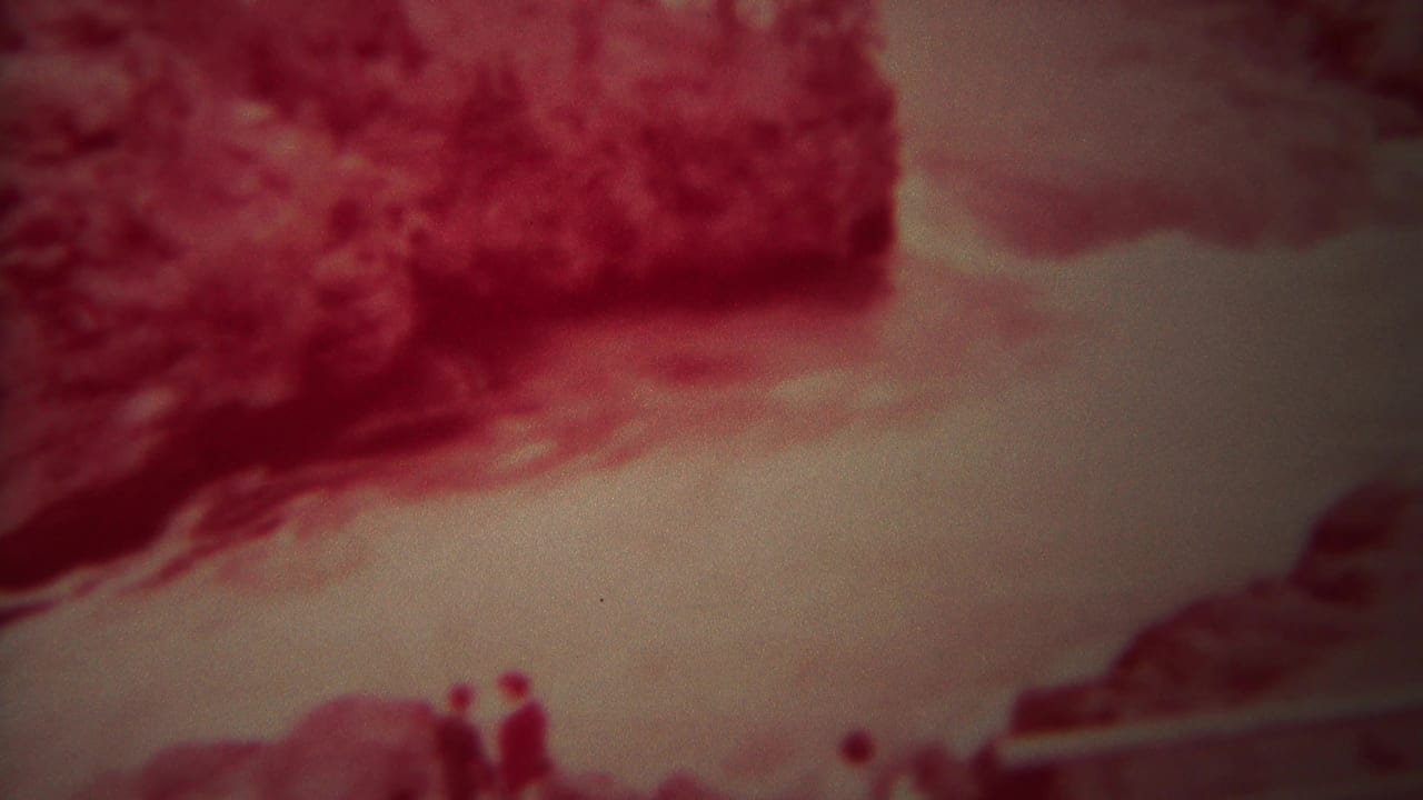 1967 Yellowstone 8mm frame showing fast pale river water, a red rocky bank, and small indistinct people near the shoreline.