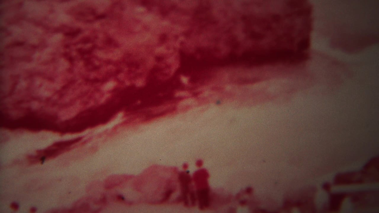 Fast pale river water with red rocky bank and tiny figures near the lower edge.