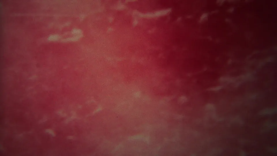 1967 Yellowstone 8mm frame of abstract rushing water, tinted red and pink with grain, blur, and darker water along the edges.