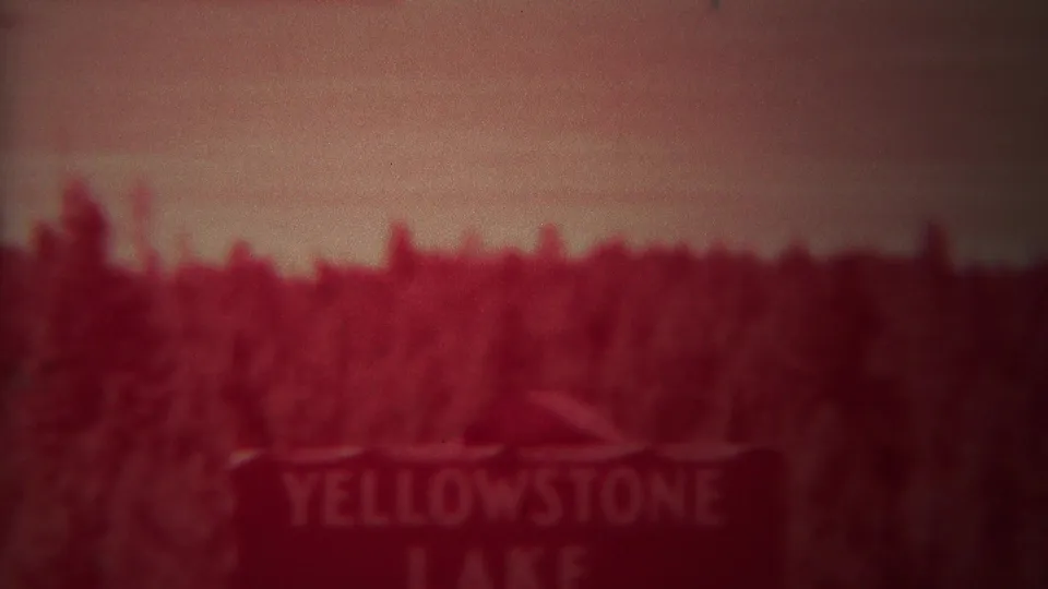 Blurred Yellowstone Lake sign framed by dense forest in 1967 8mm Yellowstone home-movie footage.