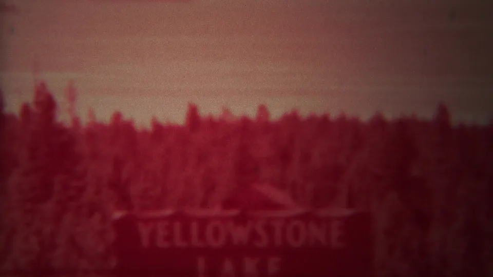 Red-tinted 1967 8mm view of the Yellowstone Lake sign with trees and sky behind it.