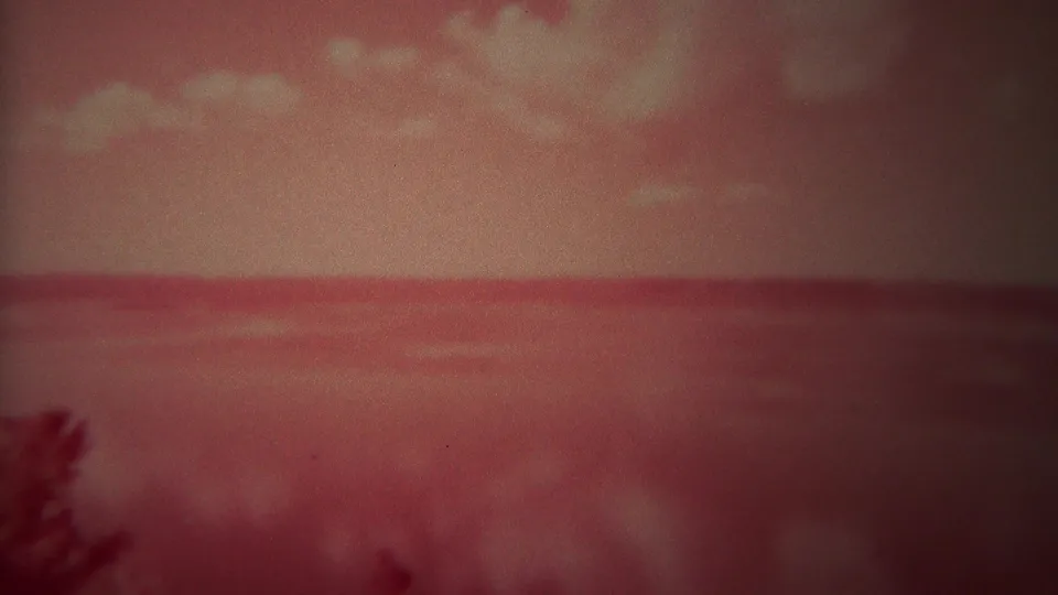1967 Yellowstone 8mm frame showing a red-tinted river or lake horizon, pale clouds, and dark foliage at the bottom of the view.