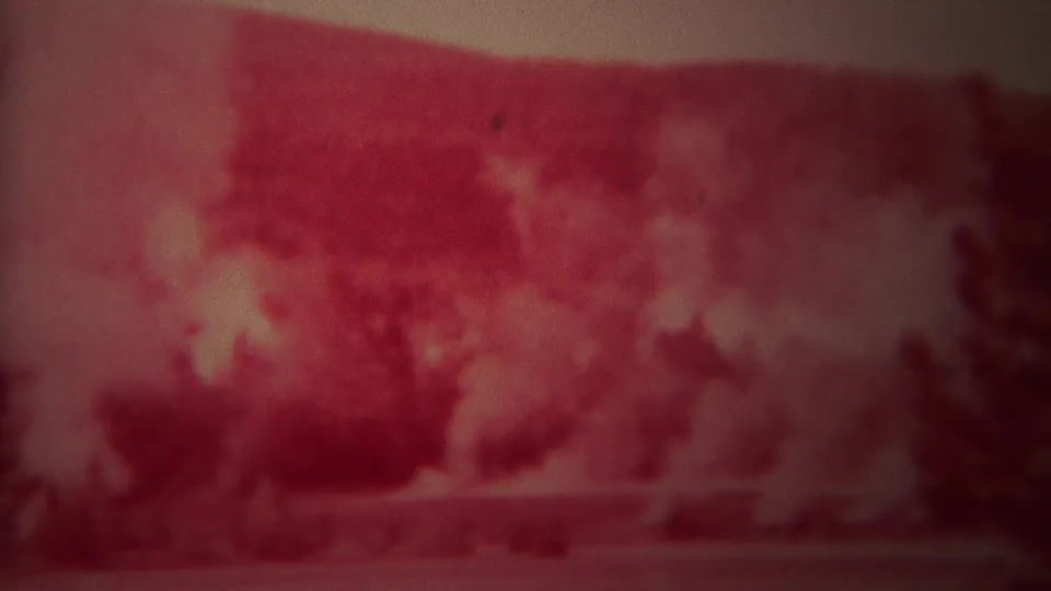 Red-faded 1967 Yellowstone frame with a blurry geothermal basin view and possible steam or haze in the distance.
