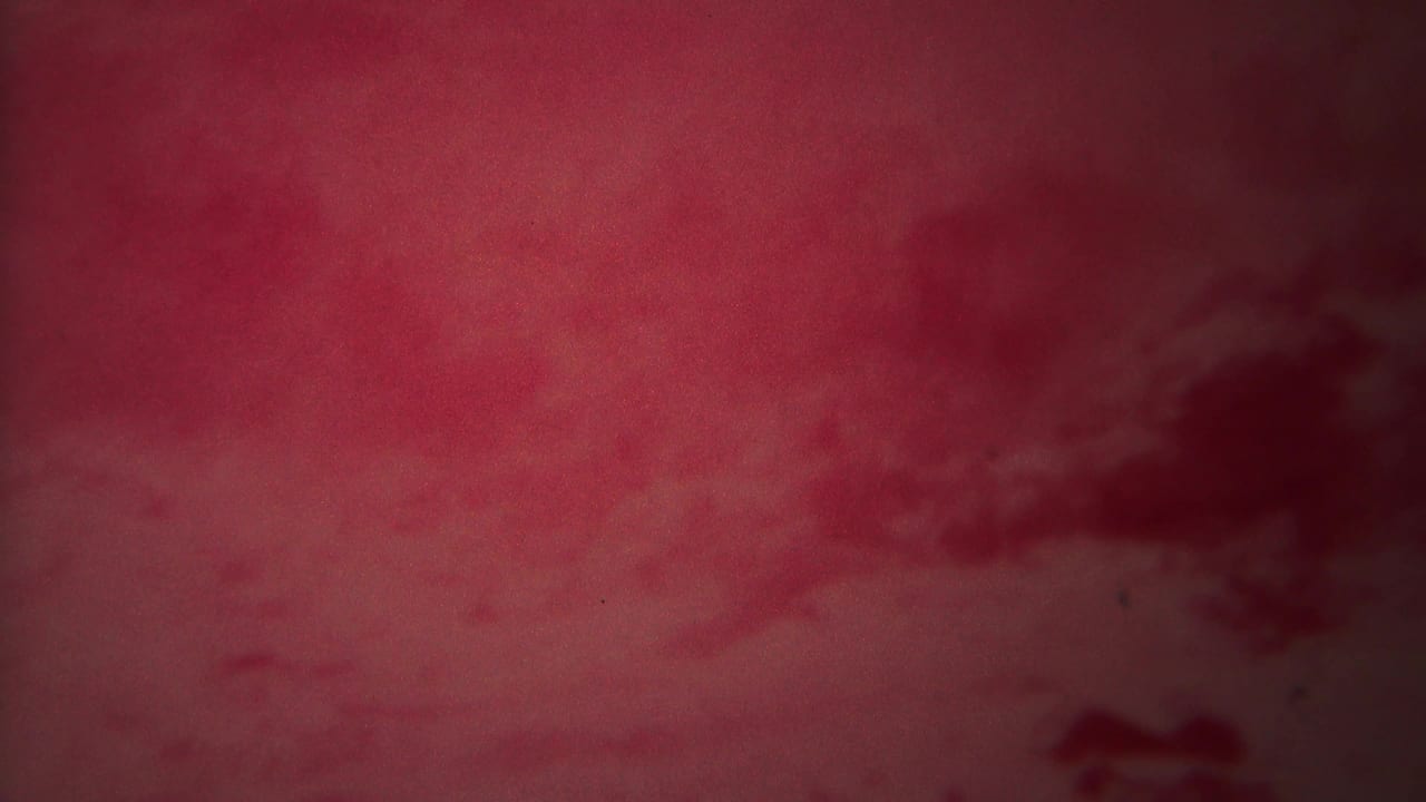 Red-tinted geothermal basin with steam, low clouds, and soft mineral flats.