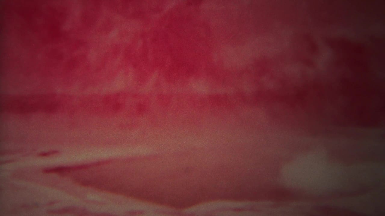 Blurred red landscape with steam haze, clouds, and distant dark ridge.
