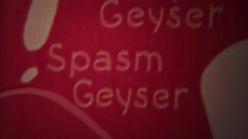 1967 Yellowstone 8mm frame showing a red title-like surface with soft yellow lettering reading Geyser Spasm Geyser.