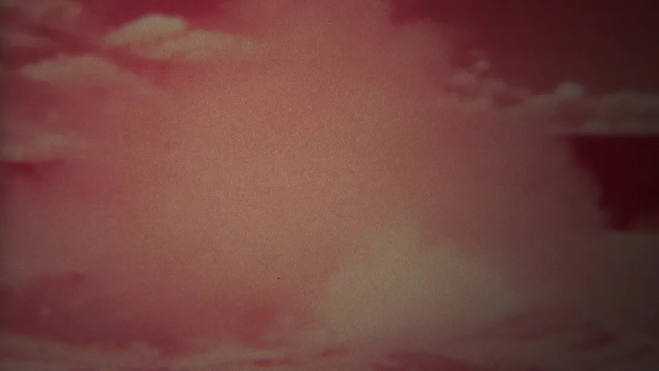 Late frame of the Yellowstone geyser eruption, with pale steam and spray filling the lower scene beneath a pink sky.