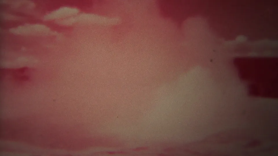 Red-cast 8mm view of clouds over a landscape, with a dark partial shape at the edge of the frame.