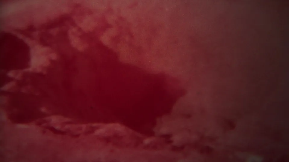 Red-shifted 8mm frame of a dark rocky or geothermal formation near pale ground in the Yellowstone clip.