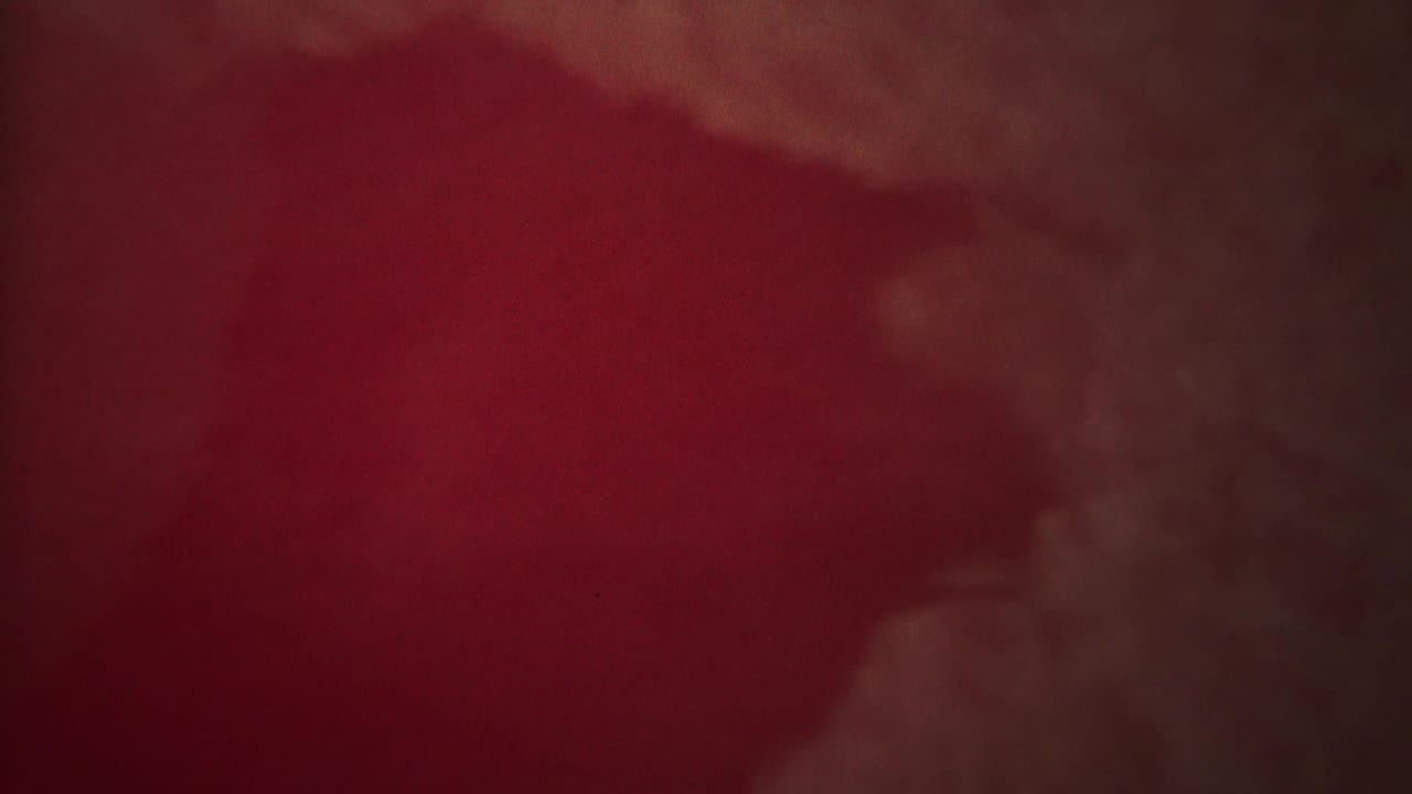 Red-tinted hazy frame with a faint pale plume shape and soft film grain.