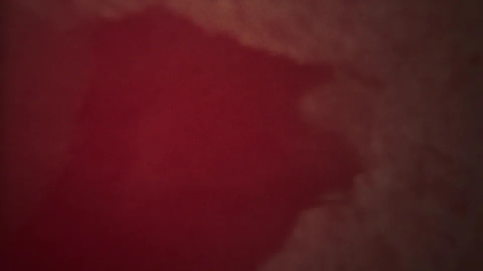 1967 Yellowstone 8mm frame with heavy red color cast, haze, and a faint pale steam or spray form emerging in soft focus.