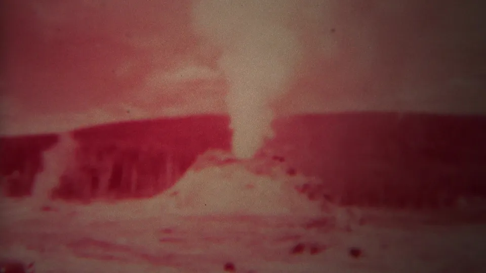 1967 Yellowstone 8mm frame with a pale steam or spray plume rising from rough ground behind a dark ridge under a reddish cast.