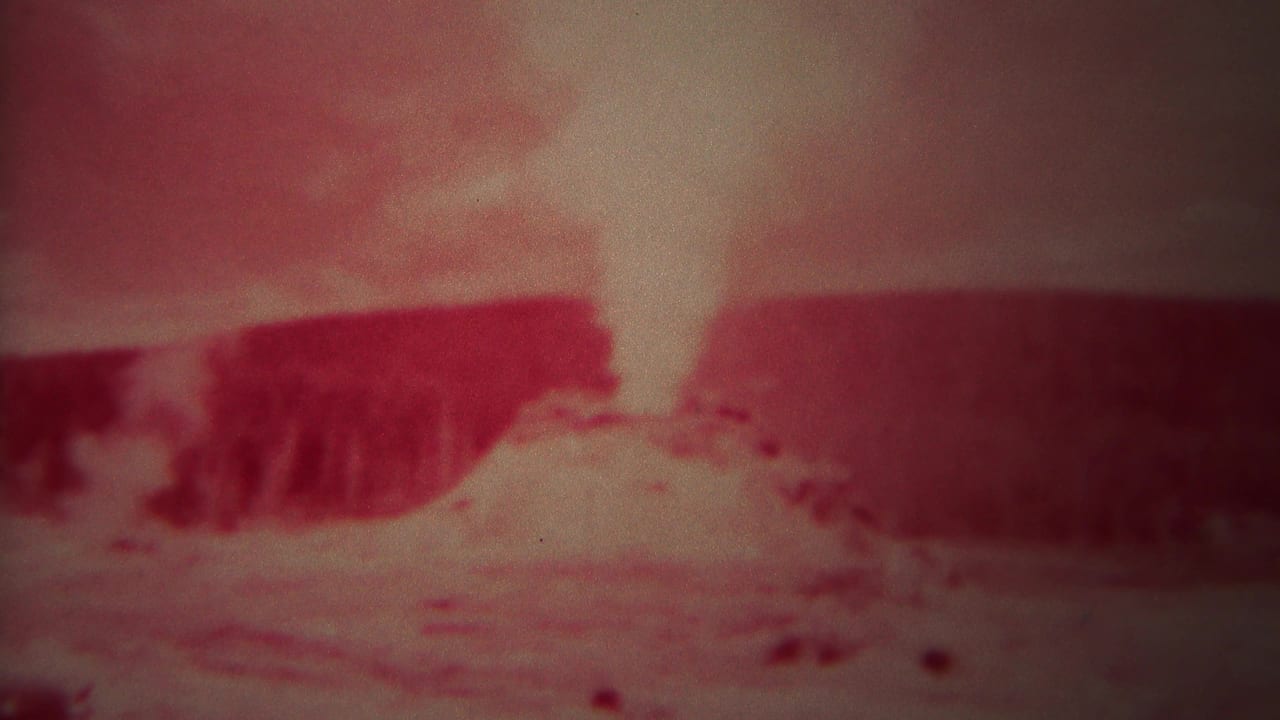 Red-tinted geyser plume rising from rocky ground.
