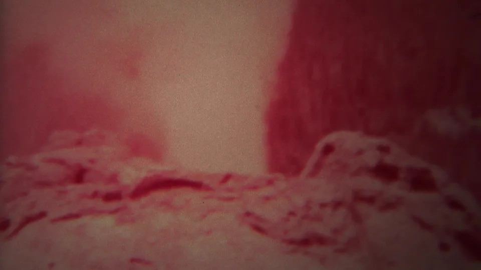 Soft 8mm Yellowstone view of steam and mineral ground near the geyser vent, tinted red by the film image.