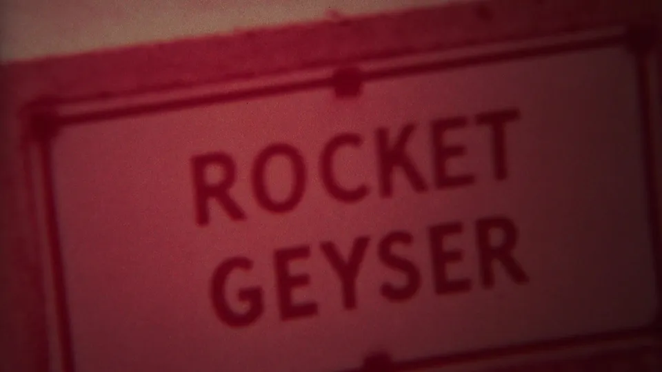 1967 Yellowstone 8mm frame showing a readable Rocket Geyser sign next to red-tinted geyser terrain.