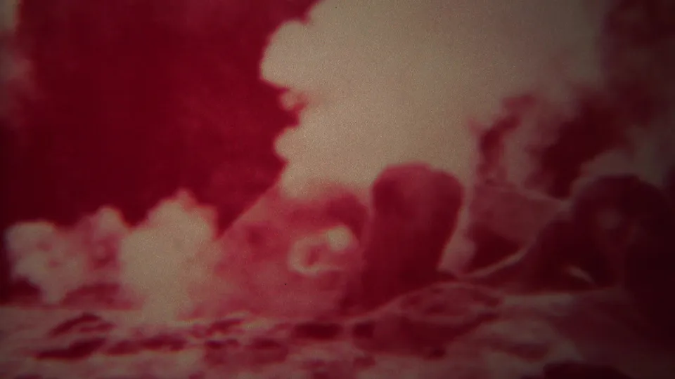 Red-tinted 8mm Yellowstone frame showing thick geyser steam around dark rock formations and a rounded vent-like shape.