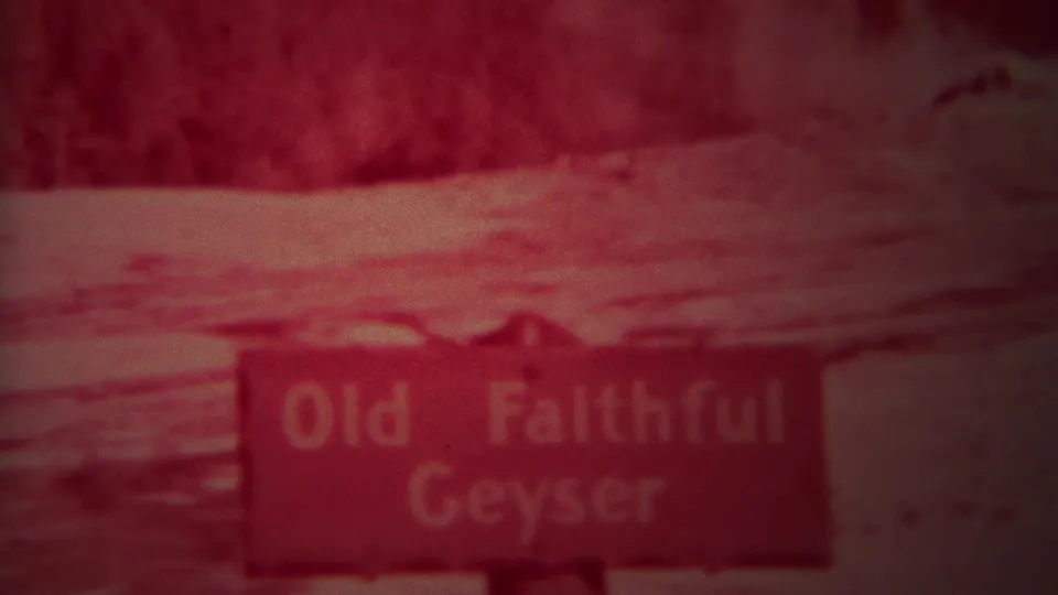 Red-tinted 1967 Yellowstone home-movie frame showing a sign reading Old Faithful Geyser near a viewing area.