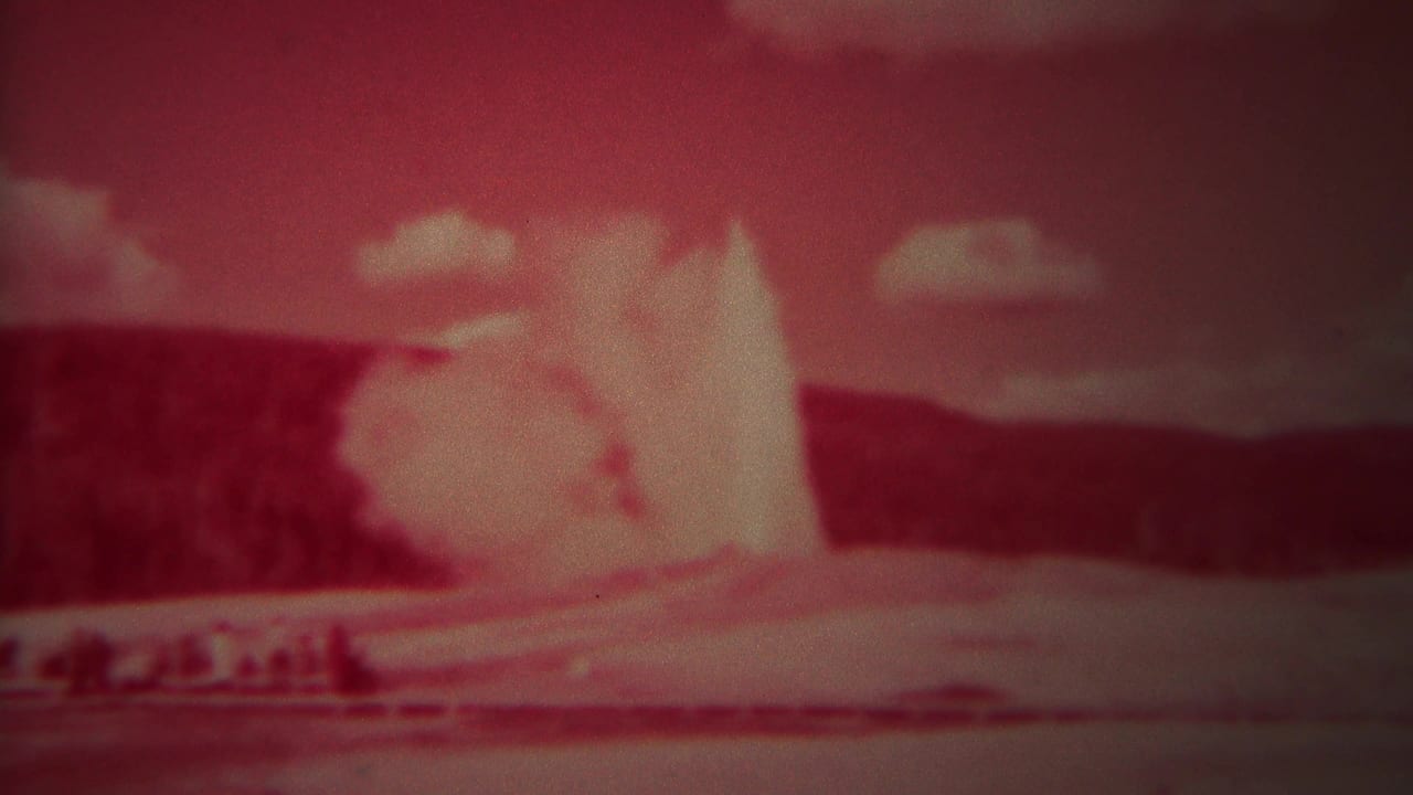Tall geyser spray rises against a red sky with a dark tree line behind it.