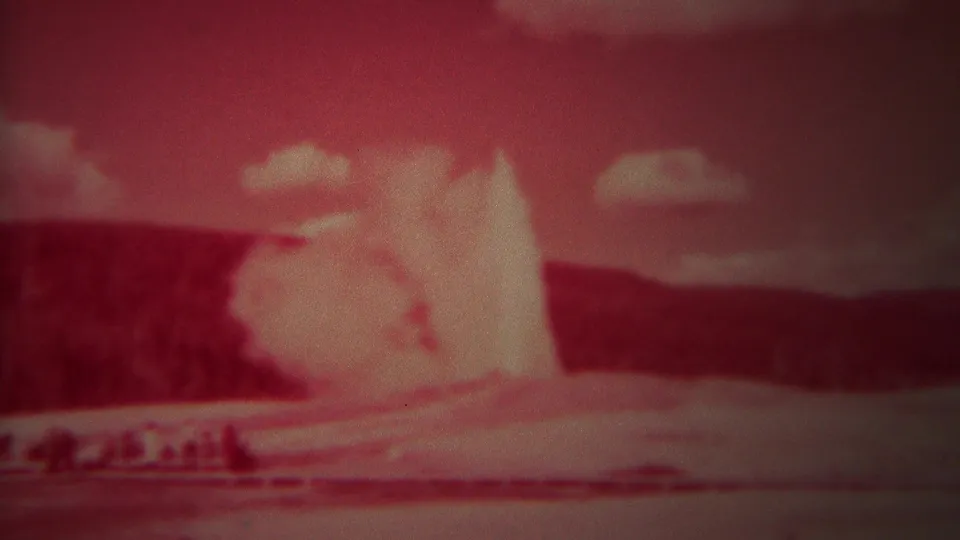 1967 Yellowstone frame with a high Old Faithful water plume, distant spectators, and strong red color shift from the 8mm film.