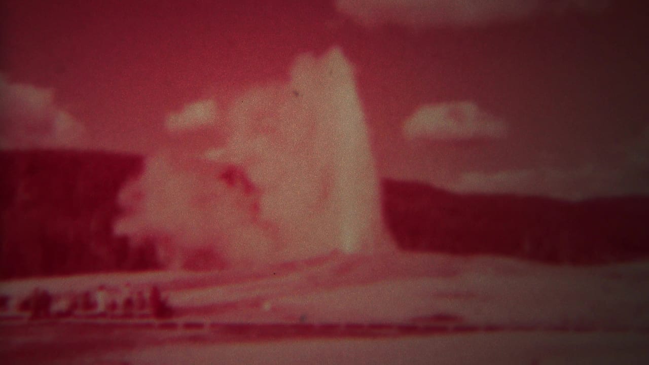 Red-tinted 8mm frame of a geyser erupting beneath a cloudy sky.