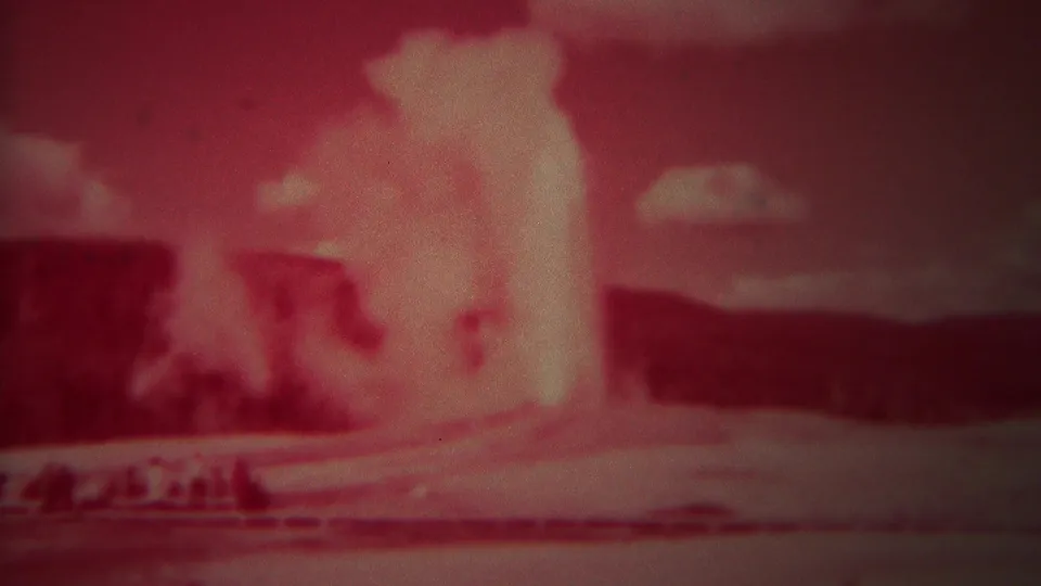 1967 Yellowstone home-movie still with Old Faithful erupting in a broad pale plume over the geyser basin.