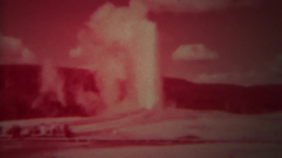 Red-tinted 1967 Yellowstone frame of Old Faithful shooting a tall plume above the geyser basin.