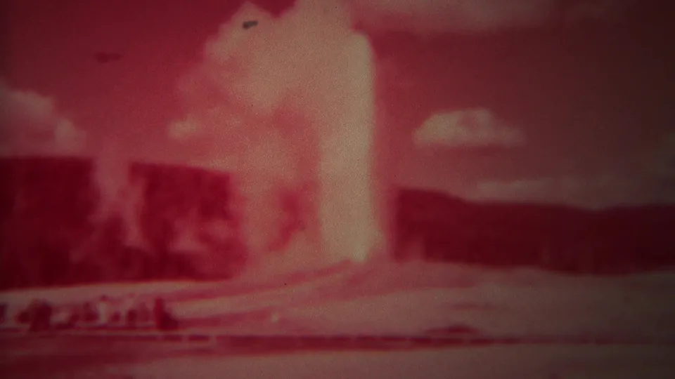 1967 Yellowstone home-movie still showing the Old Faithful plume in soft red-tinted 8mm film.
