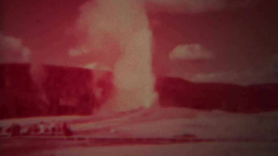 1967 Yellowstone 8mm frame showing the geyser plume continuing against dark hills with heavy red color cast.