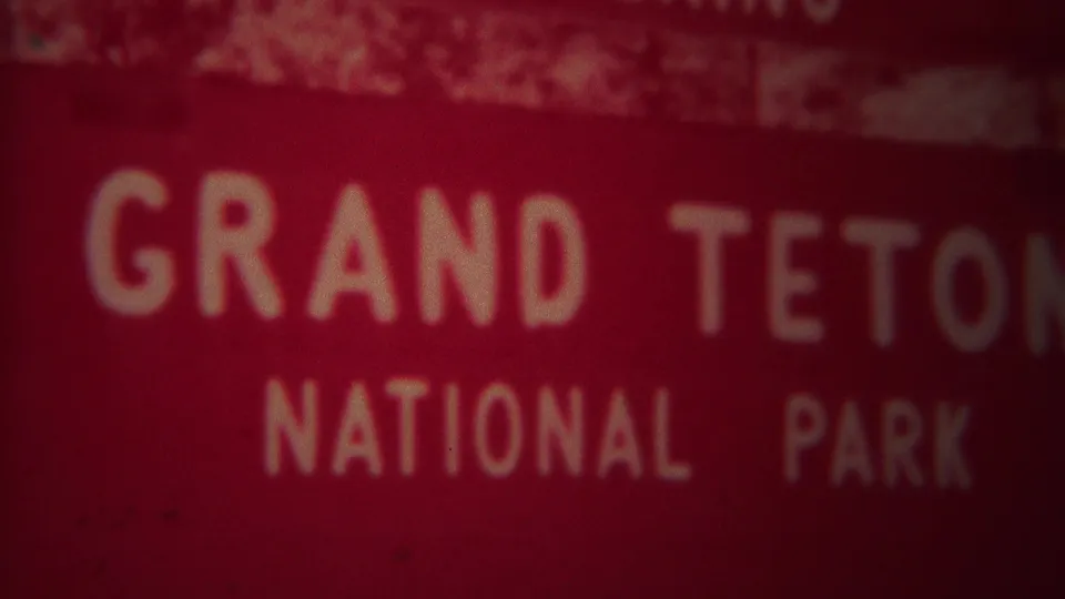 1967 8mm frame showing a blurred red Grand Teton National Park sign in Wyoming with white block lettering and heavy grain.