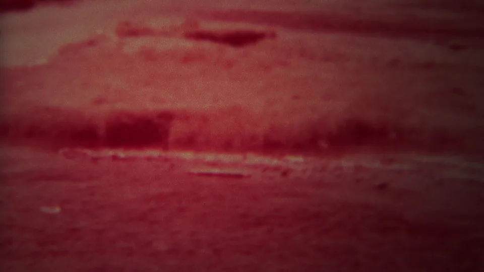1967 8mm frame with the lower sign area mostly out of focus, showing reddish ground or foreground texture below the Grand Teton sign.