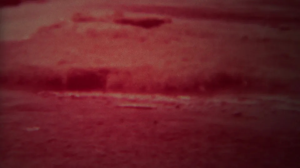 1967 8mm frame showing a blurred red foreground and dark horizontal band near the cropped Grand Teton sign scene.