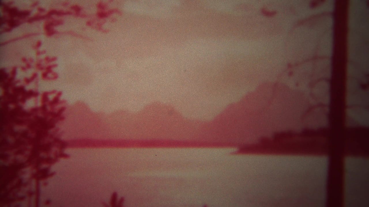 Red-tinted lake view with dark trees and distant mountains under a hazy sky.