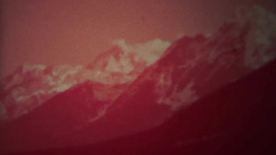 1967 Yellowstone-area home-movie frame showing rugged mountain slopes and pale snow-bright areas through red-faded film.