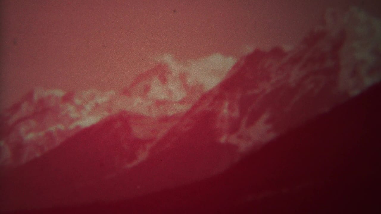 1967 Yellowstone, Wyoming 8mm frame showing red-tinted mountains, snow patches, haze, and a dark sloping foreground.