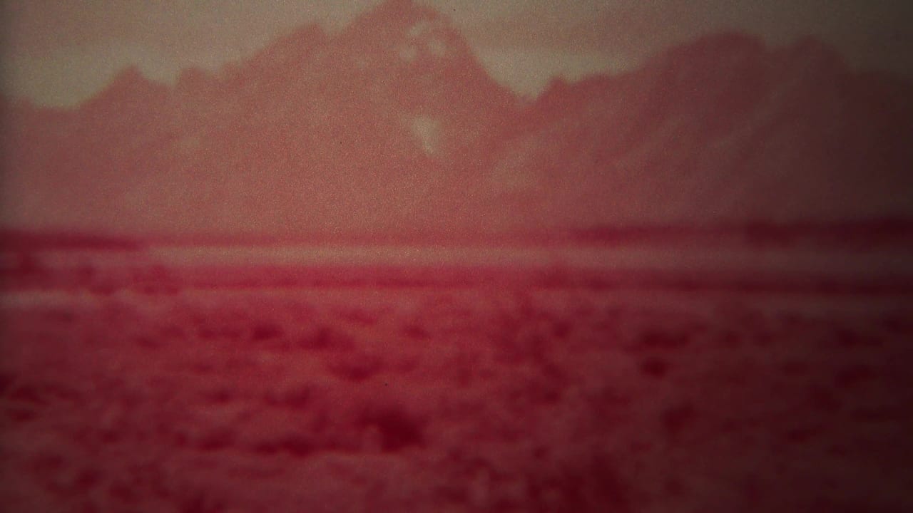 Hazy red mountain ridge beyond a broad textured plain.