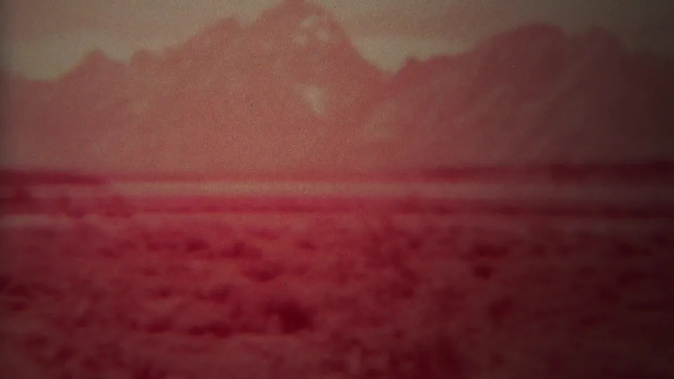 1967 Yellowstone, Wyoming landscape frame with a crimson cast over distant mountains and an open scrubby plain.
