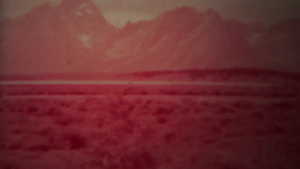 1967 Yellowstone, Wyoming 8mm frame showing a soft red mountain landscape with broad foreground texture and horizontal haze.