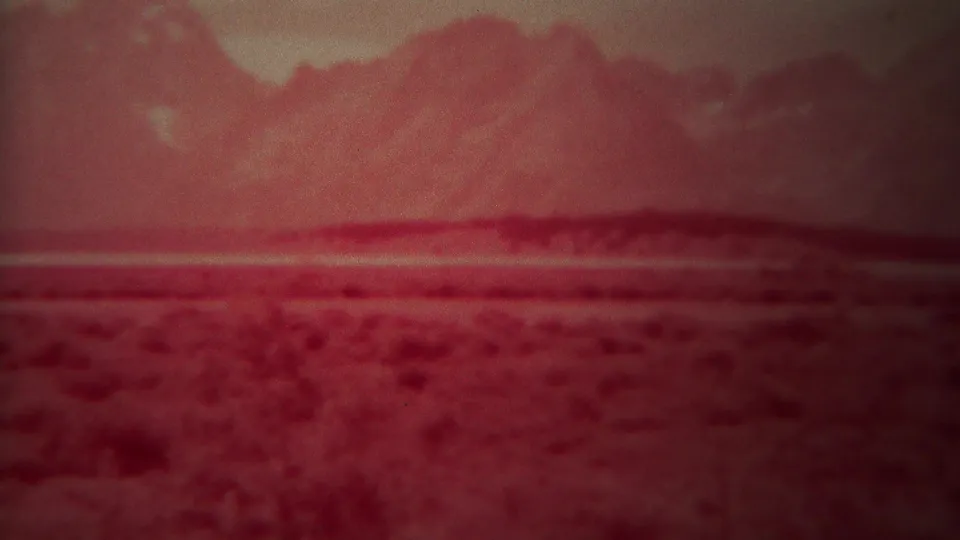 1967 Yellowstone, Wyoming closing frame with red-tinted mountain peaks, a broad plain, and pronounced 8mm grain.