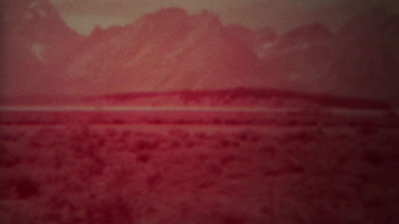 Red-tinted open plain with low scrub and distant mountains under a hazy sky.