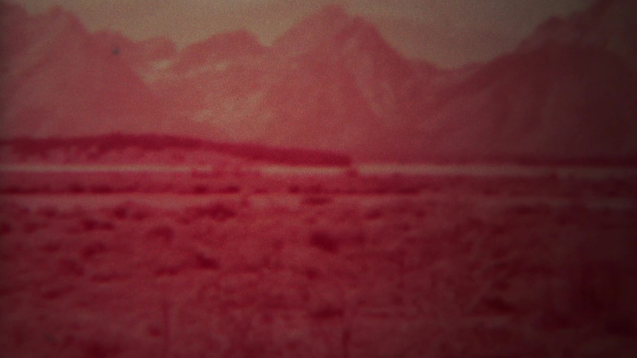 Red-tinted mountain range beyond a flat scrub-covered plain.