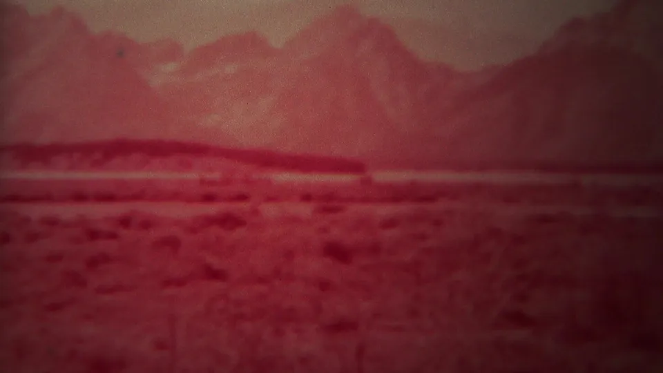 Red-tinted 1967 8mm home-movie view of distant mountains across open terrain in the Yellowstone, Wyoming area.