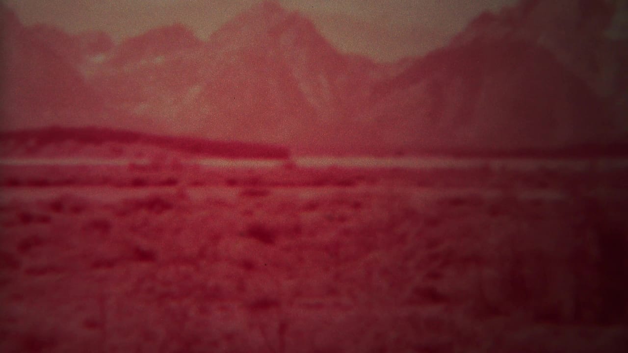 Soft red mountain landscape with open foreground and hazy horizon.