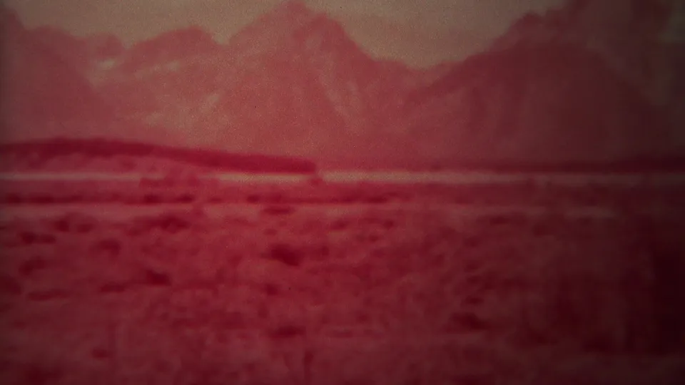 Softly focused 8mm frame showing red-tinted mountains and open ground, supported as Yellowstone, Wyoming, 1967 by clip metadata.